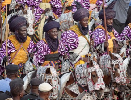 Nigeria, Kano State, Kano. Hausa men dressed in bright-coloured purple flowing robes and indigo turbans participate in a Durbar parade. Their fine horses are equally impressive, adorned with ornate ceremonial regalia.